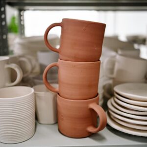 Close-up of stacked handmade ceramic mugs and plates showcasing pottery craft in a studio setting.